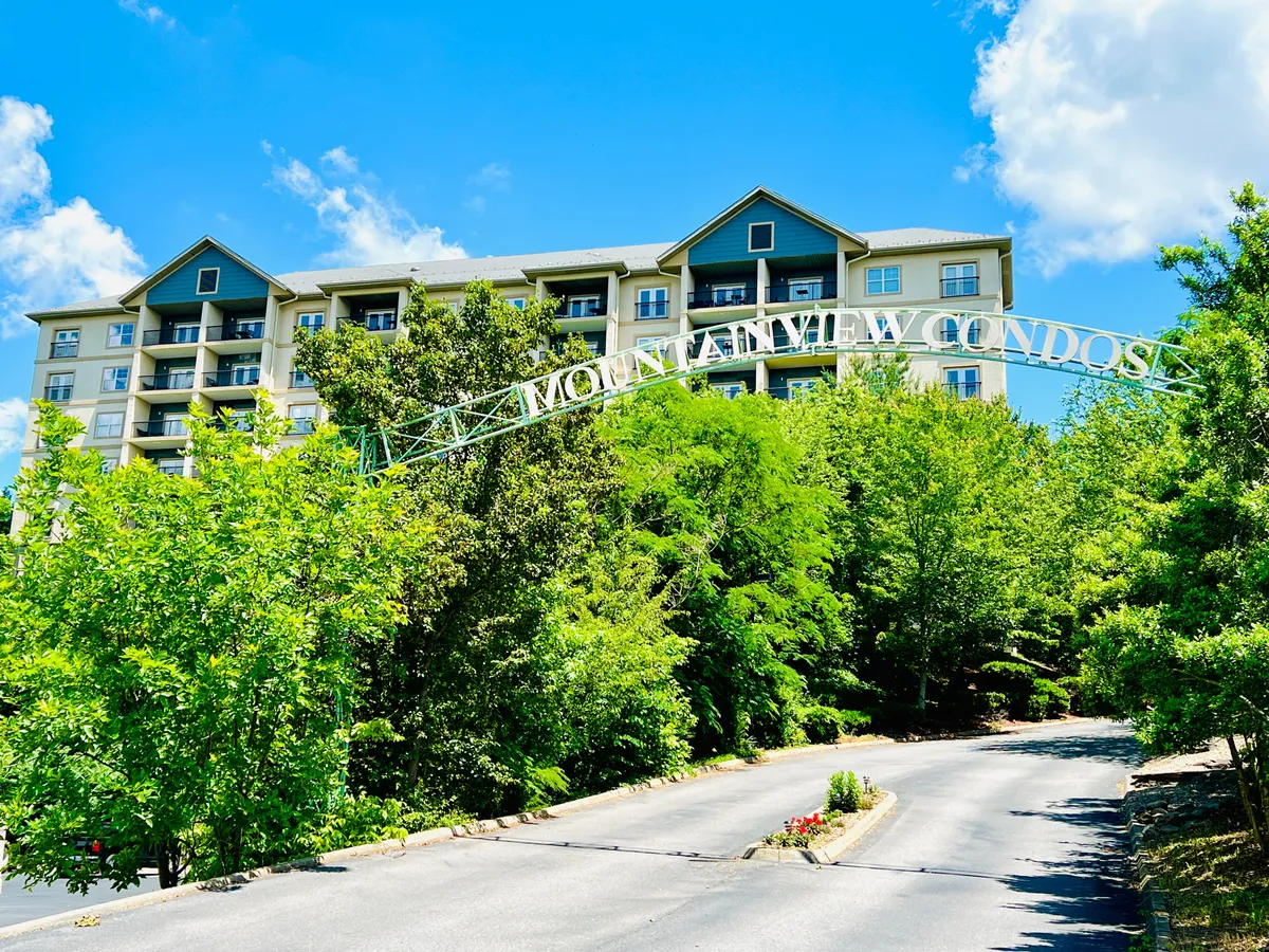 A welcoming view of the Mountain View Condos sign set against the backdrop of the building structure, surrounded by lush greenery. The image hints at the property's proximity to nature and its namesake mountain scenery.
