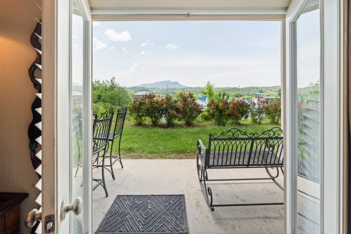 A scenic patio area featuring inviting outdoor seating, lush greenery, and a breathtaking view of the Smoky Mountains in the distance. The scene evokes peaceful mornings or tranquil evenings spent with a loved one while surrounded by nature.