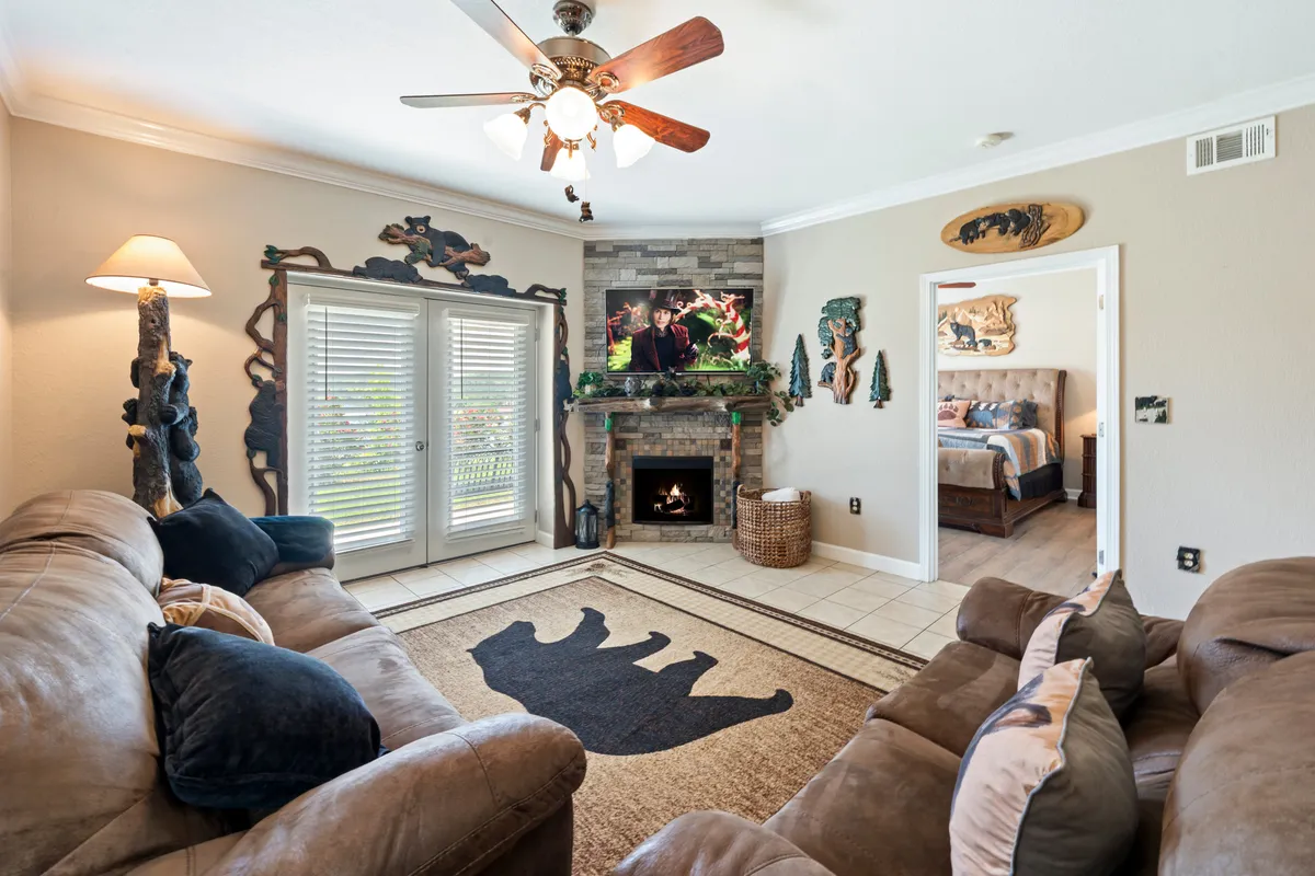 A comfortable living room featuring a plush sofa seating area, a bear-shaped rug, a warm fireplace, decorative wall art, and a flat-screen TV. The space exudes rustic mountain-modern décor and is arranged to encourage relaxation and togetherness.
