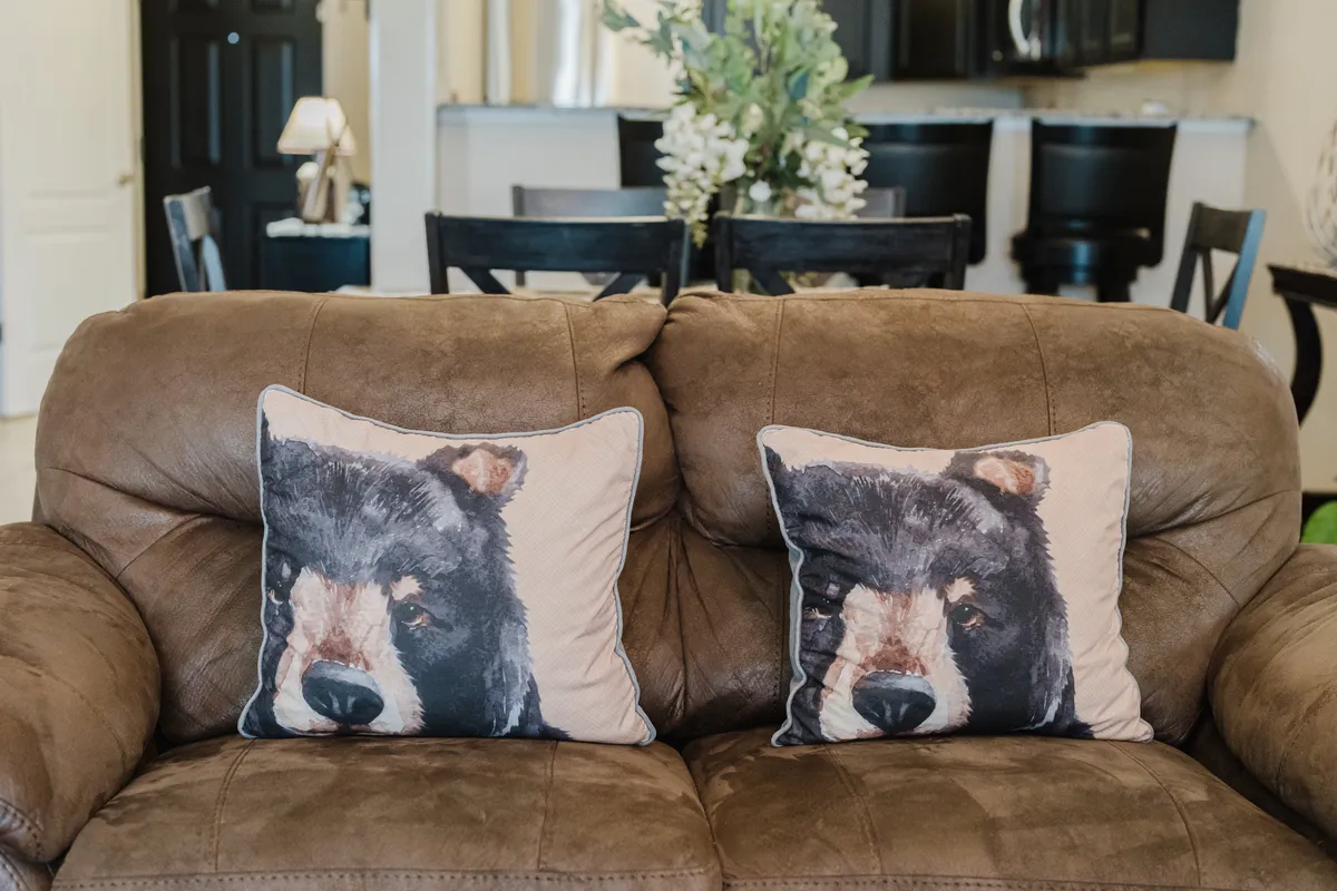 A close-up view of a comfortable sofa adorned with bear-themed throw pillows and a decorative bouquet of flowers on the coffee table, set against a warm, inviting interior backdrop.