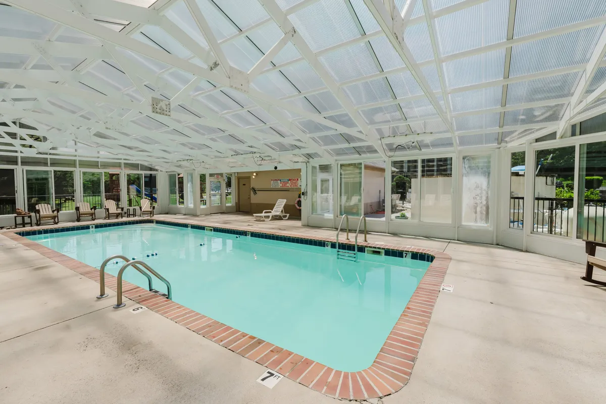 An indoor swimming pool with comfortable seating and a glass ceiling letting in natural light. The area is designed for relaxation, socializing, and group fun, whether you're taking a dip or lounging poolside.