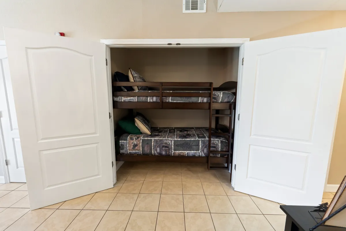 A cozy set of bunk beds with plush pillows and soft lighting, nestled into a small space with tiled flooring, evoking a playful and intimate sleepover atmosphere for kids or extra guests.