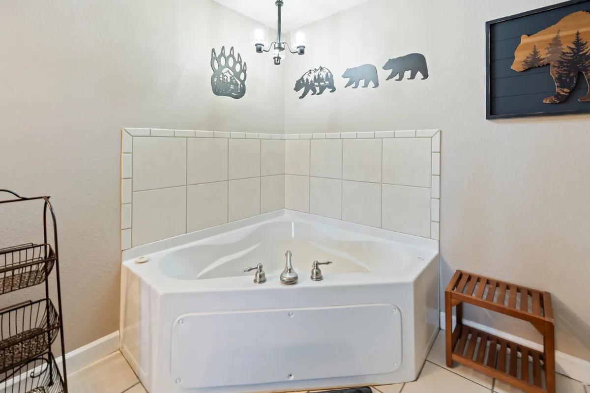 A tranquil interior featuring a jacuzzi tub with bear-themed wall decor and a warm chandelier above, evoking a spa-like ambiance. The scene suggests a private, rejuvenating space perfect for couples to unwind together after a day outdoors.