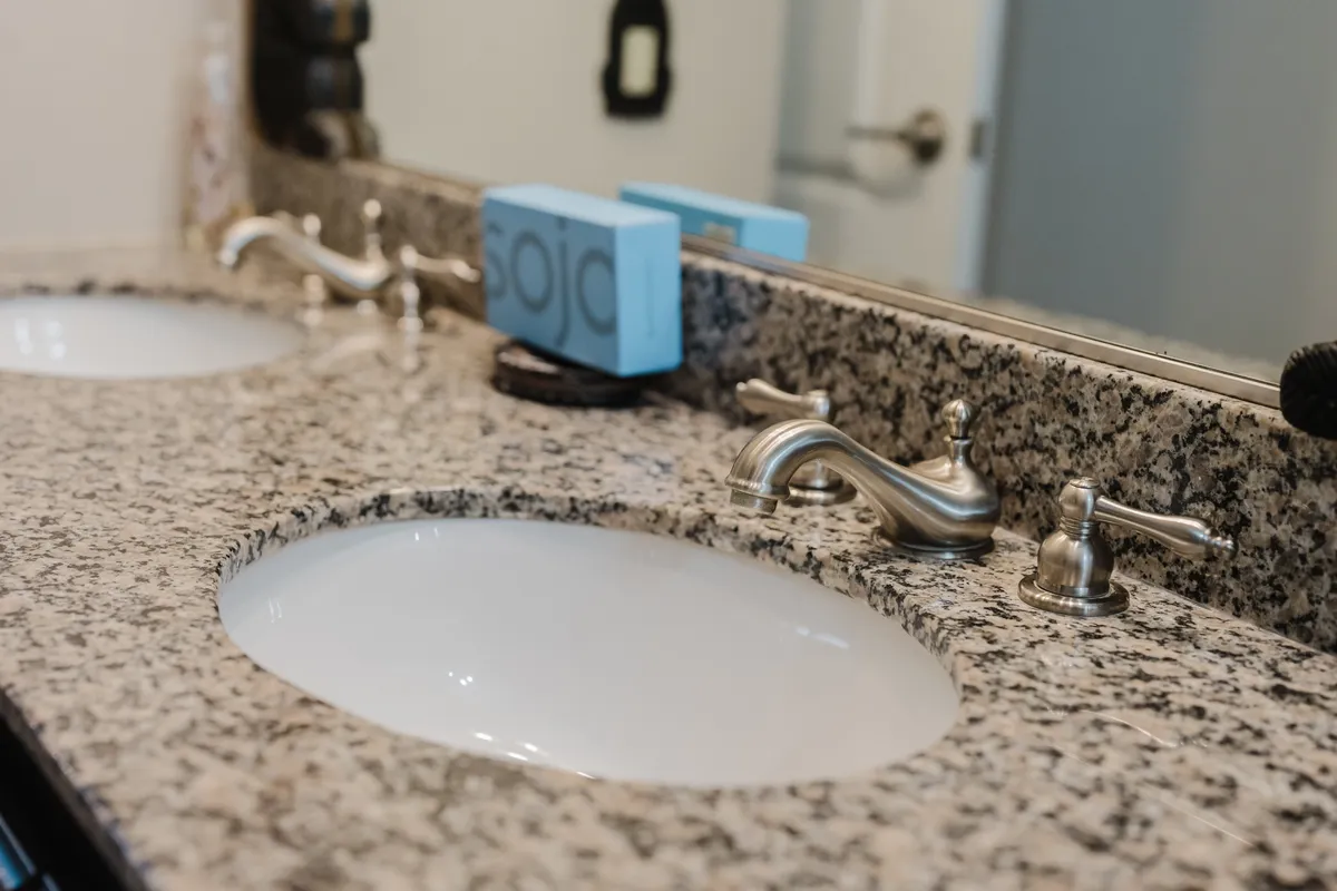 A modern bathroom vanity with dual sinks and sleek fixtures, topped by a granite countertop and a decorative blue box, offering ample space for morning routines and self-care.