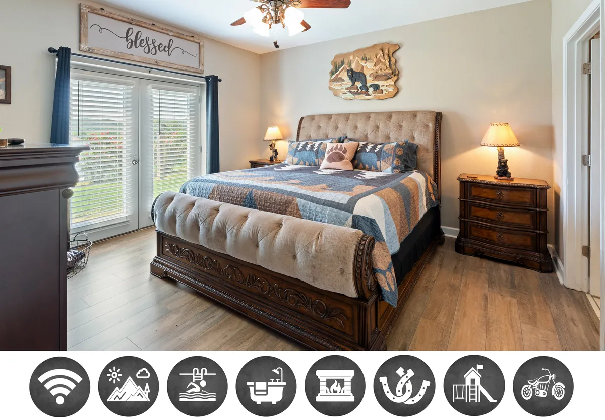 The image showcases a cozy, inviting bedroom inside the condo. The bed is adorned with plush, decorative pillows, flanked by warm-lit nightstands and soft lamps, while a window dressed in gentle curtains lets in natural light. Wood accents above the bed reflect a charming, mountain-inspired decor, creating a serene space perfect for relaxation.