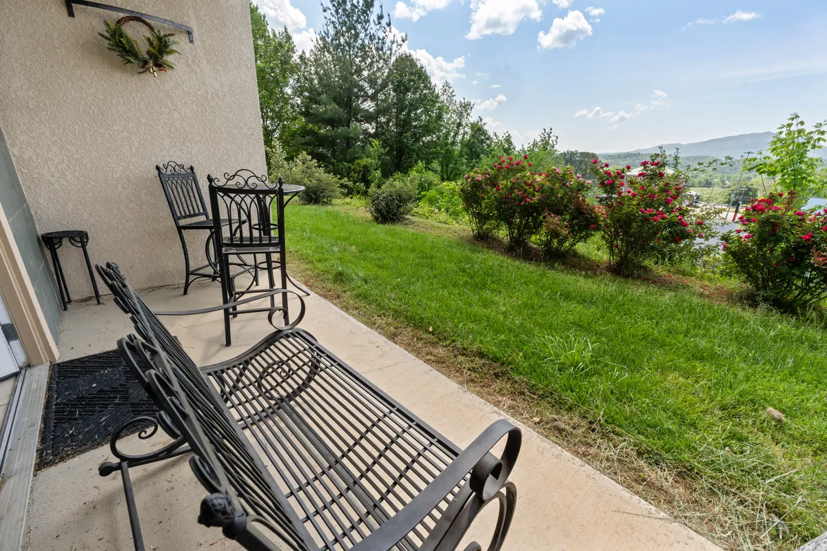 A serene patio scene featuring wrought iron chairs, a well-maintained lawn, flowering bushes, and a spectacular view of the distant mountains. The setting is peaceful, inviting residents to relax while immersed in nature.