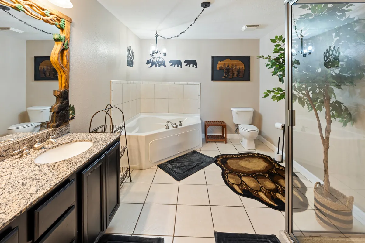 A luxurious bathroom featuring a large jacuzzi tub set against a granite countertop, accented with bear-themed artwork and an indoor plant, all illuminated by soft lighting for a spa-like feel.